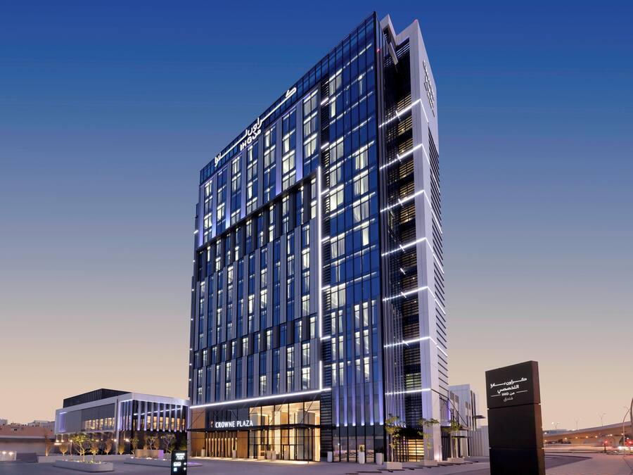 A modern hotel with a prominent glass facade, multiple floors, and a well-lit entrance.
