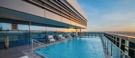 A rooftop pool with lounge chairs, a glass balustrade, and a view of the cityscape.