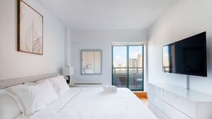 Habitación de hotel moderna con una cama grande, televisor de pantalla plana, balcón con vista a la ciudad y una obra de arte con hojas enmarcada en la pared.