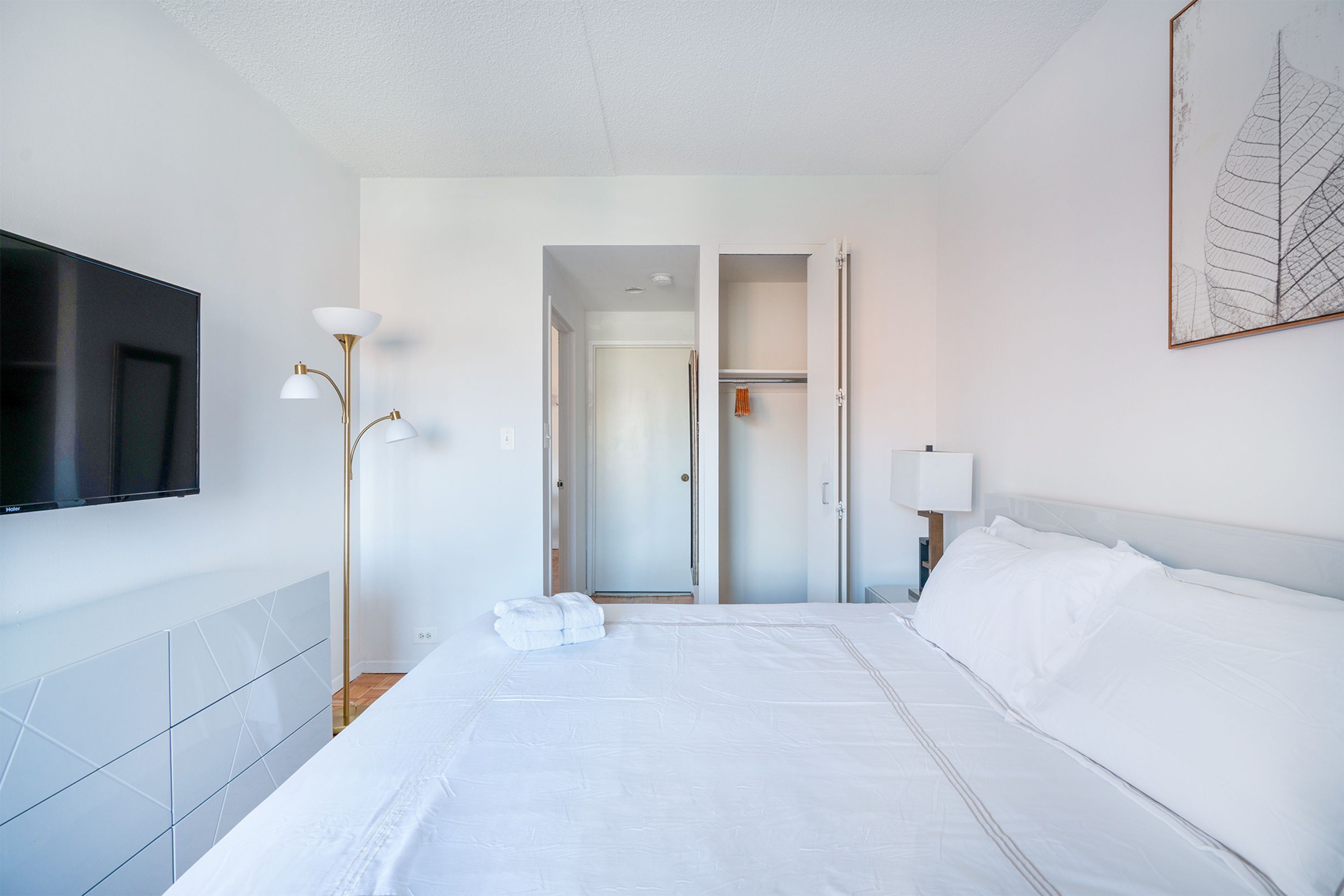 Habitación de hotel con una cama grande, un televisor de pantalla plana, una lámpara de noche y una puerta que da a un armario.