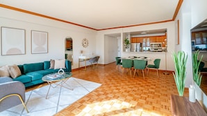 A modern living room with a wooden floor, a teal sofa, and a dining area with green chairs. - Contemporary 2 Bed 2 Bath Apt Bright and Sunny (New York)