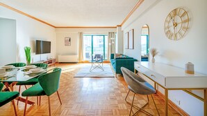 A modern living room with a dining area, a sofa, a TV, and a large clock on the wall. - Contemporary 2 Bed 2 Bath Apt Bright and Sunny (New York)