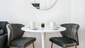 A modern dining area with a round white table, two grey upholstered chairs, and a small potted plant. - 1 BR Gem in Prime Location of NYC (New York)