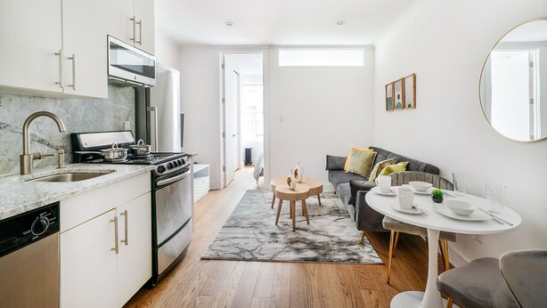 A modern kitchen with a built-in oven, microwave, and dishwasher. There is a dining area with a round table and chairs, and a sofa in the background. - 1 BR Gem in Prime Location of NYC (New York)