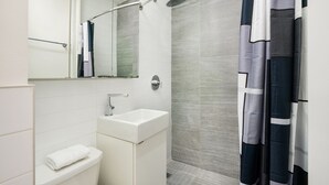 A modern bathroom with a white sink, a mirror, and a shower with a grey tiled wall. - 1 BR Gem in Prime Location of NYC (New York)