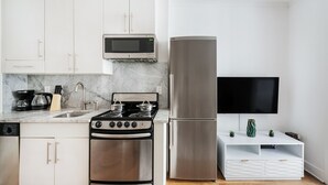 A modern kitchen with stainless steel appliances, a built-in microwave, and a flat-screen TV on a white cabinet. - 1 BR Gem in Prime Location of NYC (New York)
