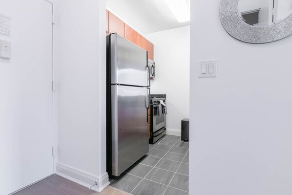 A kitchen with a stainless steel refrigerator, wooden cabinets, a microwave, and a tiled floor. - Fully Furnished 1BR in Murray Hills (New York)