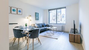A modern living room with a dining area, a sofa, a coffee table, and a TV stand. - Fully Furnished 1BR in Murray Hills (New York)