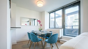 A modern dining area with a glass table, blue upholstered chairs, and a potted orchid. - Bright 2 Bedrooms 2 Bathrooms Unit With Balcony (New York)