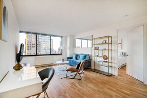 A modern living room with a sofa, coffee table, and a desk. Large windows offer a view of the cityscape. - Luxury 2 Bed 2 Bath Unit in Prime Location of NYC (New York)