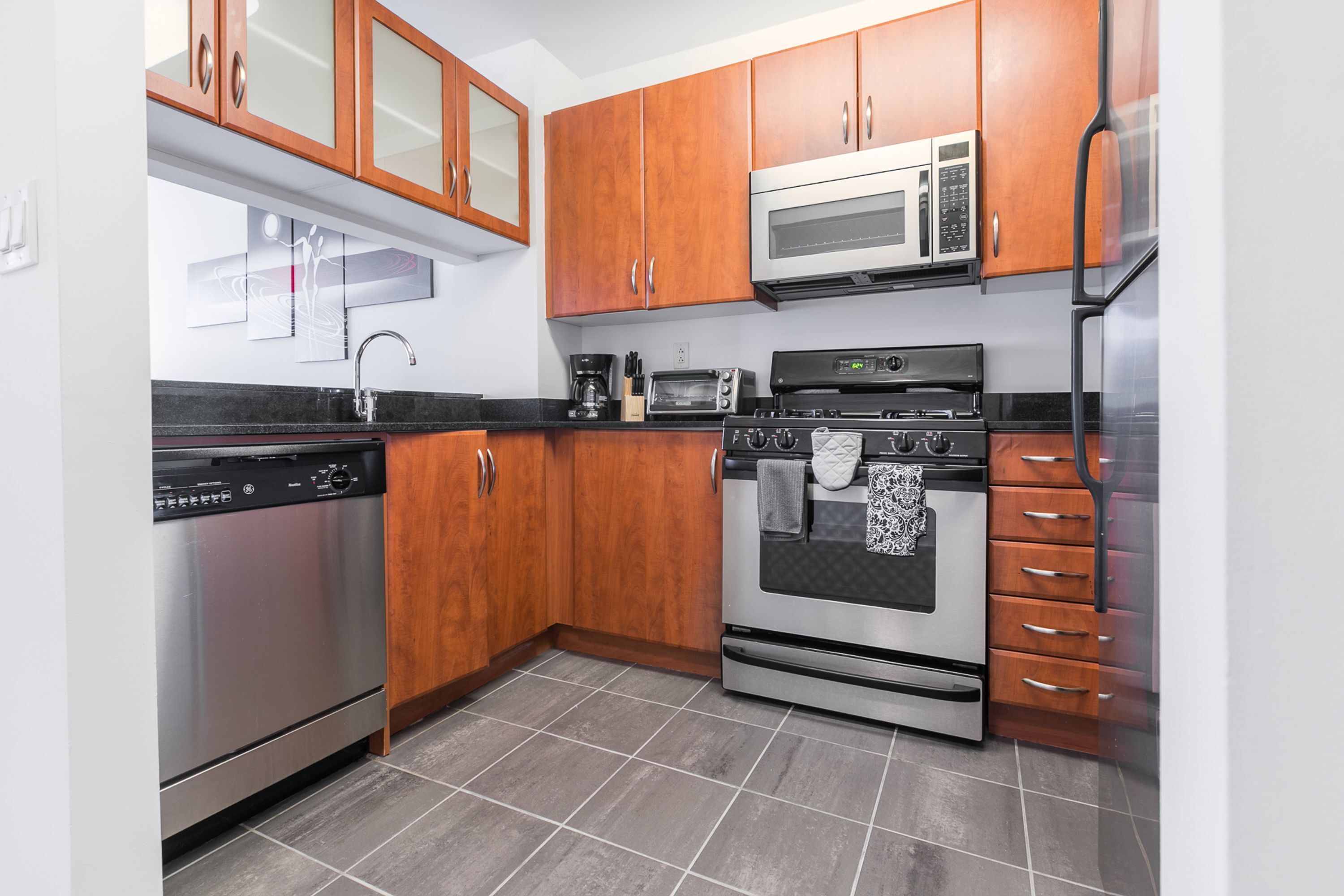 A kitchen with wooden cabinets, stainless steel appliances, and a tiled floor.