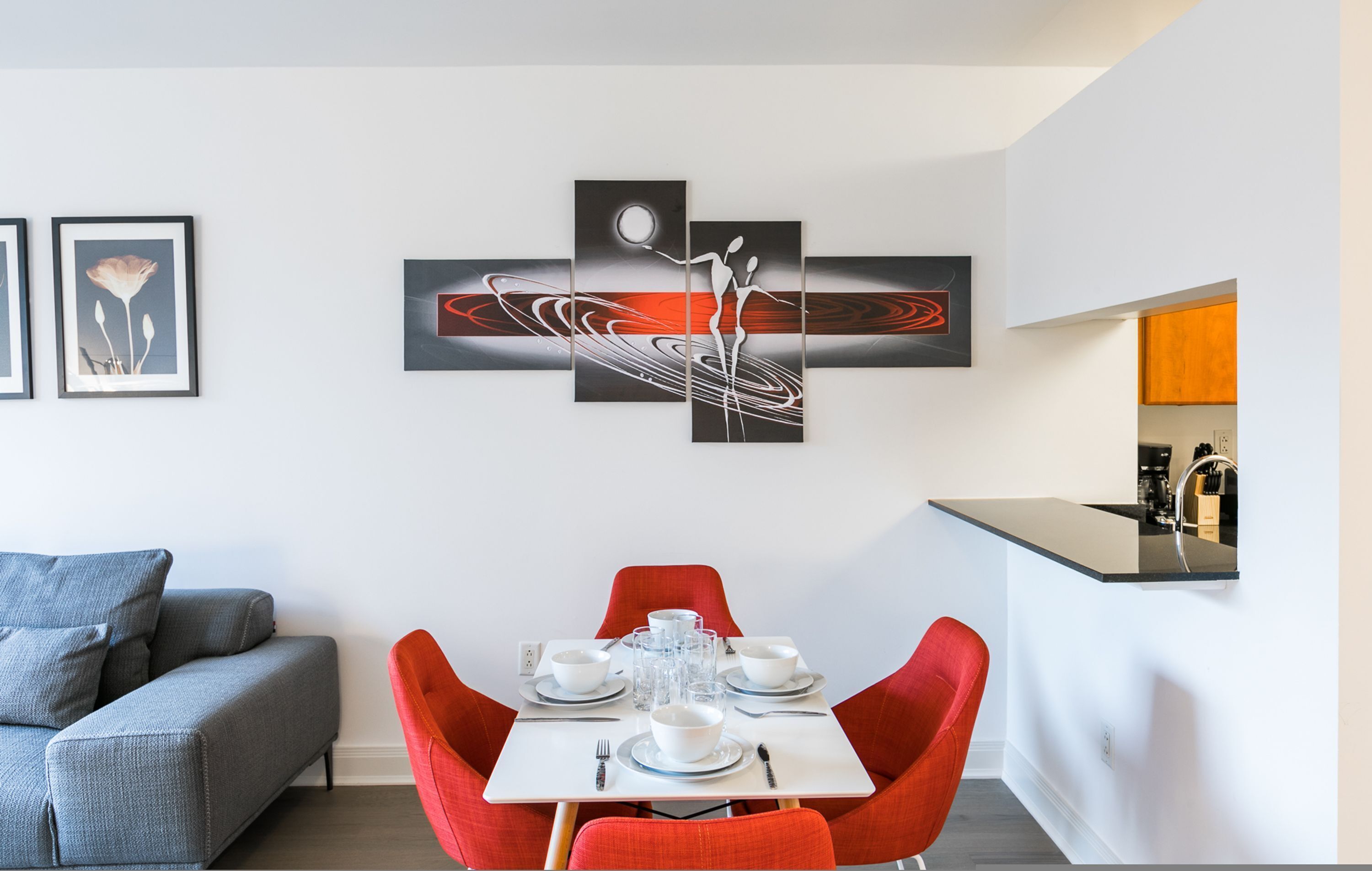A modern dining area with a table set for four, red chairs, and a contemporary art piece above the table.