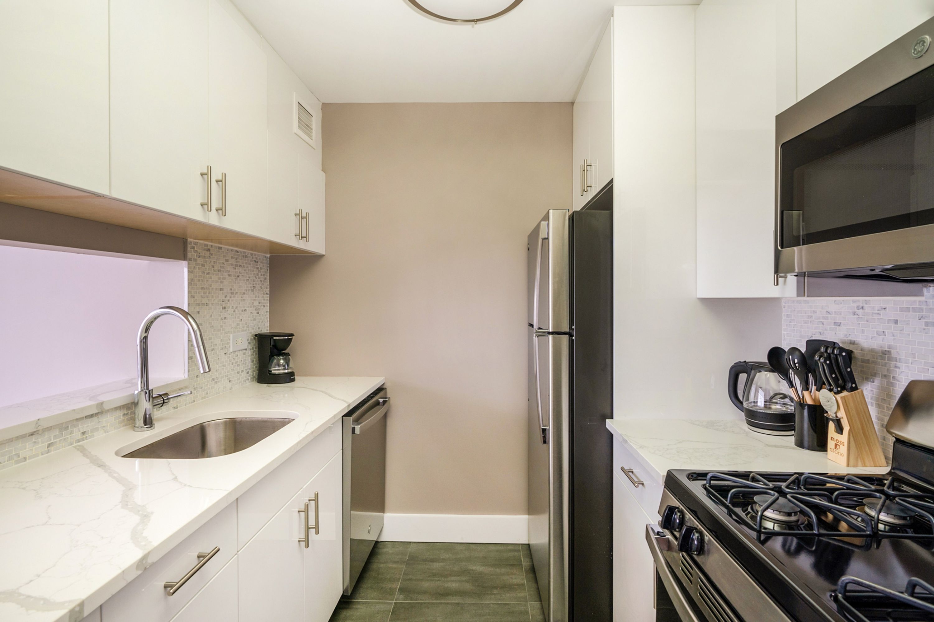 A modern kitchen with white cabinets, a stainless steel refrigerator, a gas stove, and a microwave.