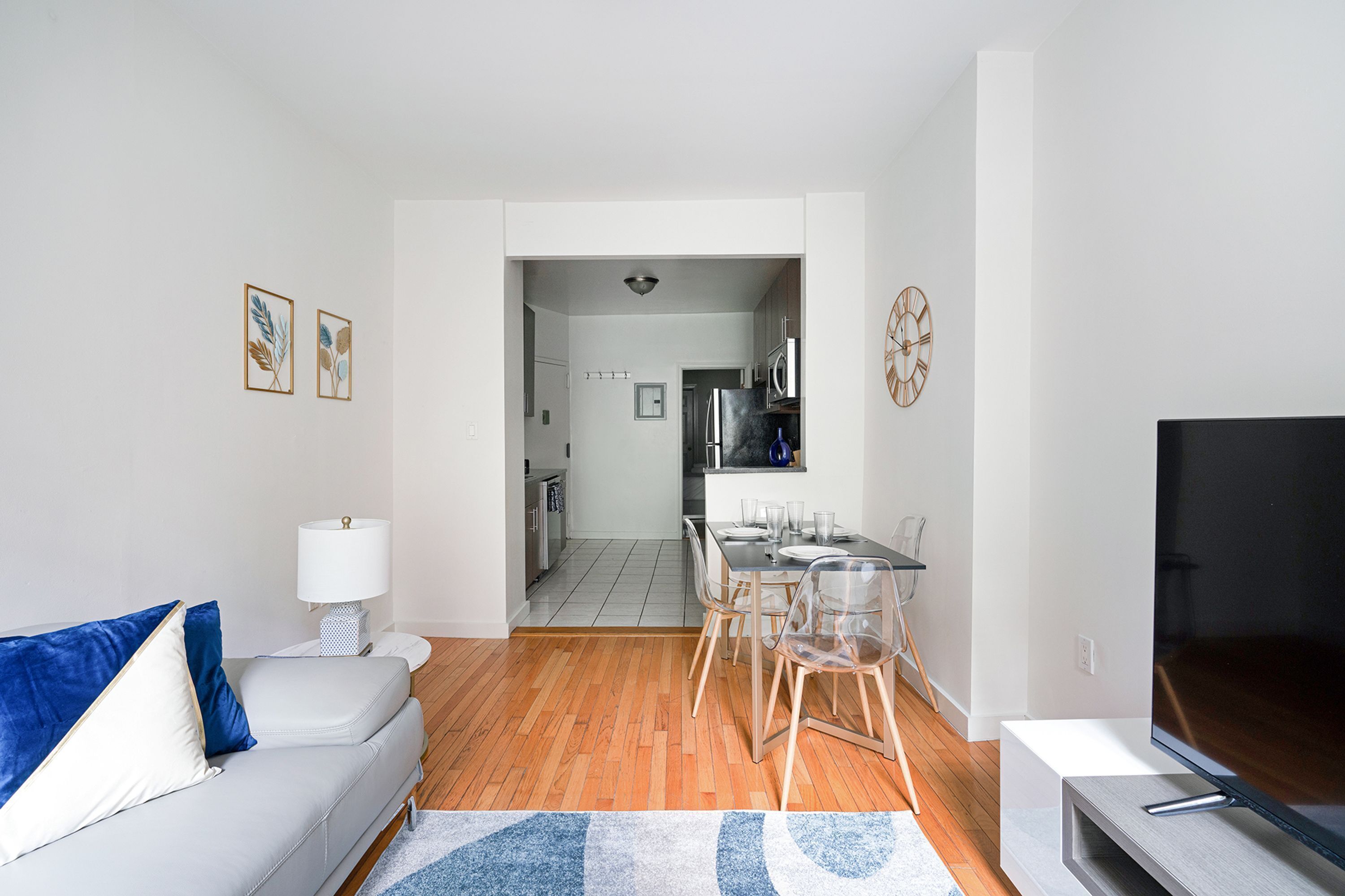 A modern living room with a white sofa, a TV, and a dining area with chairs and a table.