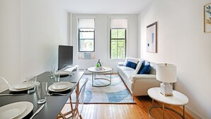 A modern living room with a dining area, featuring a sofa, coffee table, and a TV. - Prime Upper West Side Location 1 Bedroom Apt (New York)
