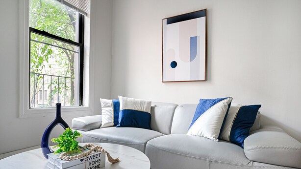 A modern living room with a white leather sofa, a round coffee table, and a framed abstract artwork on the wall. - Prime Upper West Side Location 1 Bedroom Apt (New York)