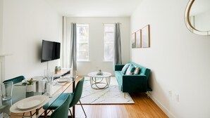 Un salon moderne comprenant un coin repas, un canapé vert et un téléviseur à écran plat.