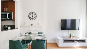 Une cuisine moderne équipée d’un four à micro-ondes, d’une horloge et d’un coin repas avec une table en verre et des chaises de couleur turquoise.