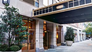 A hotel entrance with a covered walkway, large potted plants, and a prominent sign above the entrance. - Fully Furnished Studio Apartment (New York)