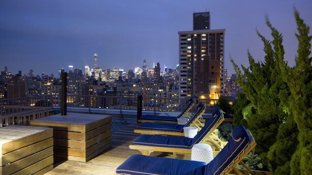 A rooftop lounge with sun loungers and a city skyline view. - Fully Furnished Studio Apartment (New York)