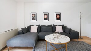 Ein modernes Wohnzimmer mit einem grauen Ecksofa, einem runden Couchtisch und drei gerahmten Kunstwerken an der Wand.
