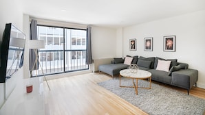 Ein modernes Wohnzimmer mit einem grauen Sofa, einem runden Couchtisch und einem großen Fenster mit Vorhängen.