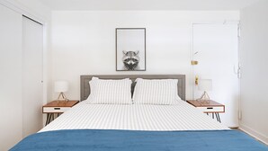 Ein Schlafzimmer mit einem Bett, zwei Nachttischen, einem gerahmten Bild an der Wand und einer Tür.