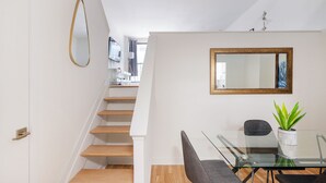 Ein modernes Interieur mit einer Treppe, einem Essbereich mit einem Glastisch, Stühlen und einer Topfpflanze.