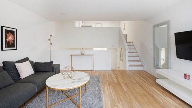 Ein modernes Wohnzimmer mit einem grauen Sofa, einem runden Couchtisch und einer Treppe, die zu einer oberen Ebene führt.