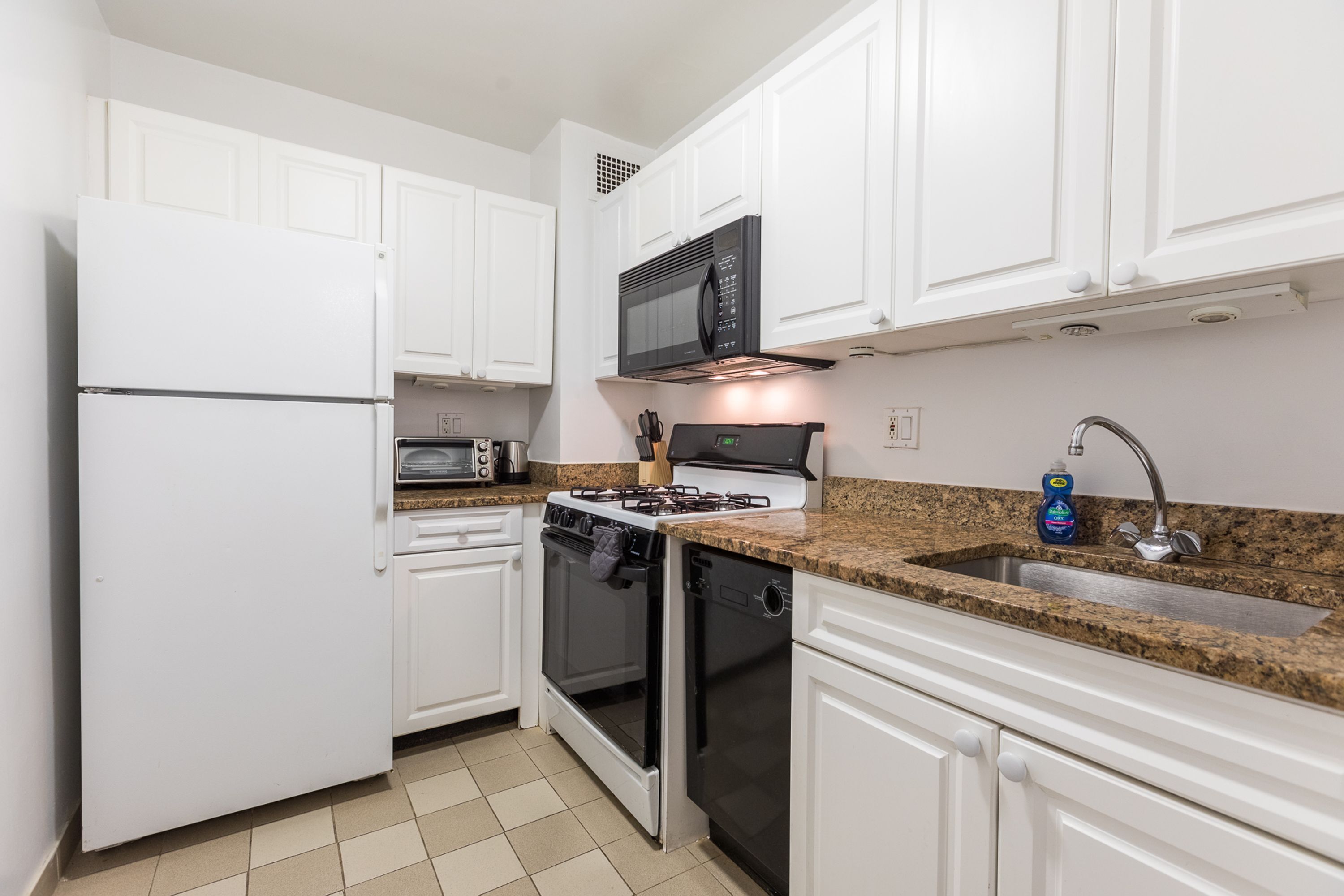 A modern kitchen with white cabinets, a microwave, stove, oven, dishwasher, and a granite countertop sink.