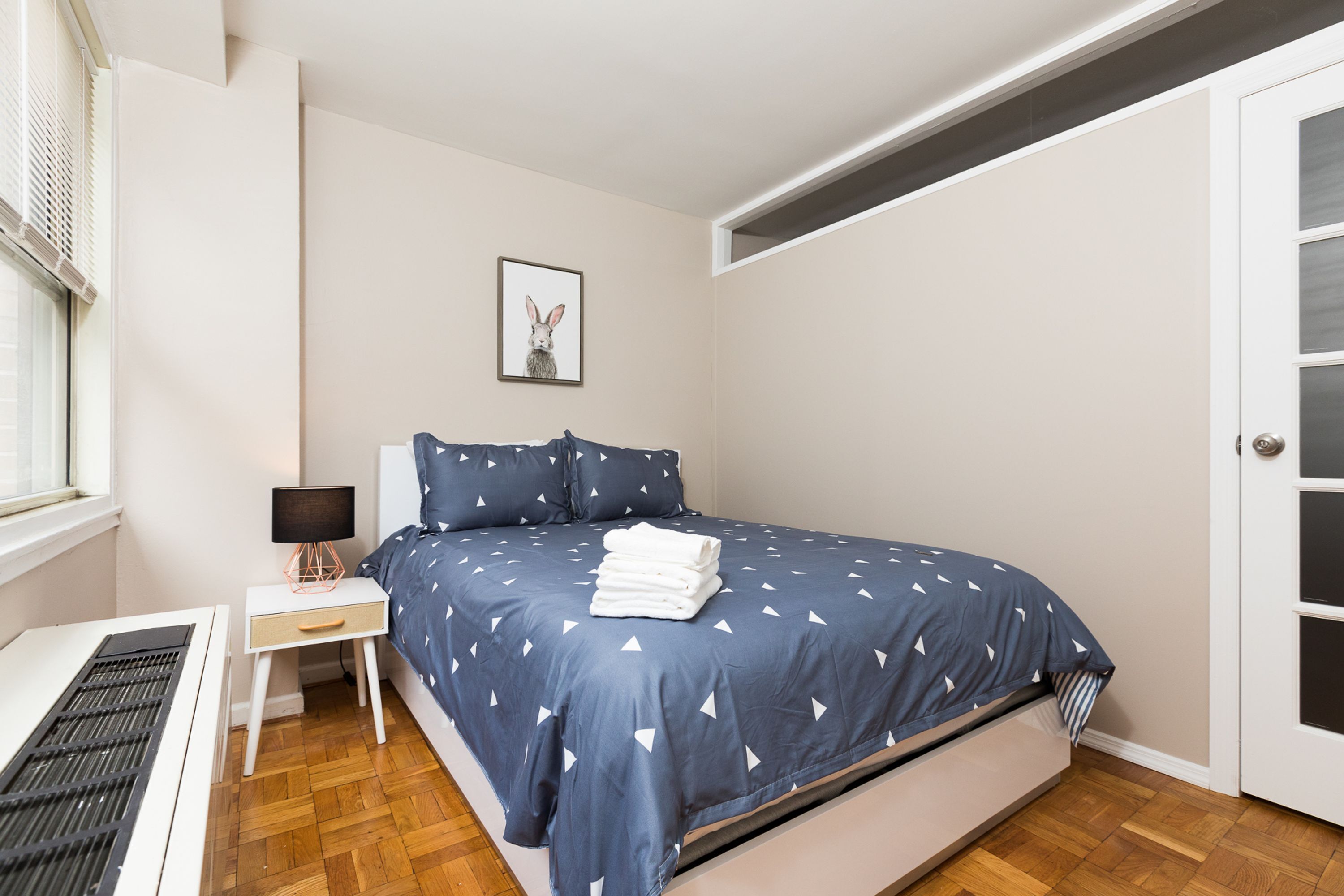 Une chambre à coucher avec un lit, une table de chevet, une lampe, un radiateur et une porte.