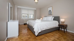A bedroom with a bed, bedside lamps, a bedside table, a radiator, a window, and a mirror. - 2 Bed Apt Ideally Located in UES of Manhattan (New York)