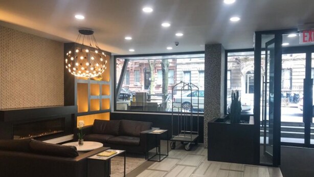 A modern lobby with a sofa, coffee table, and a decorative light fixture. - 2 Bed Apt Ideally Located in UES of Manhattan (New York)