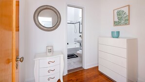 Een badkamer met een wit wastafelmeubel, een ronde spiegel en een plant in een lijst aan de muur.