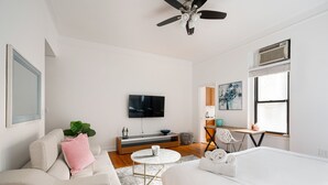 Een moderne hotelkamer met een bed, een bank, een televisie, een bureau en een plafondventilator.