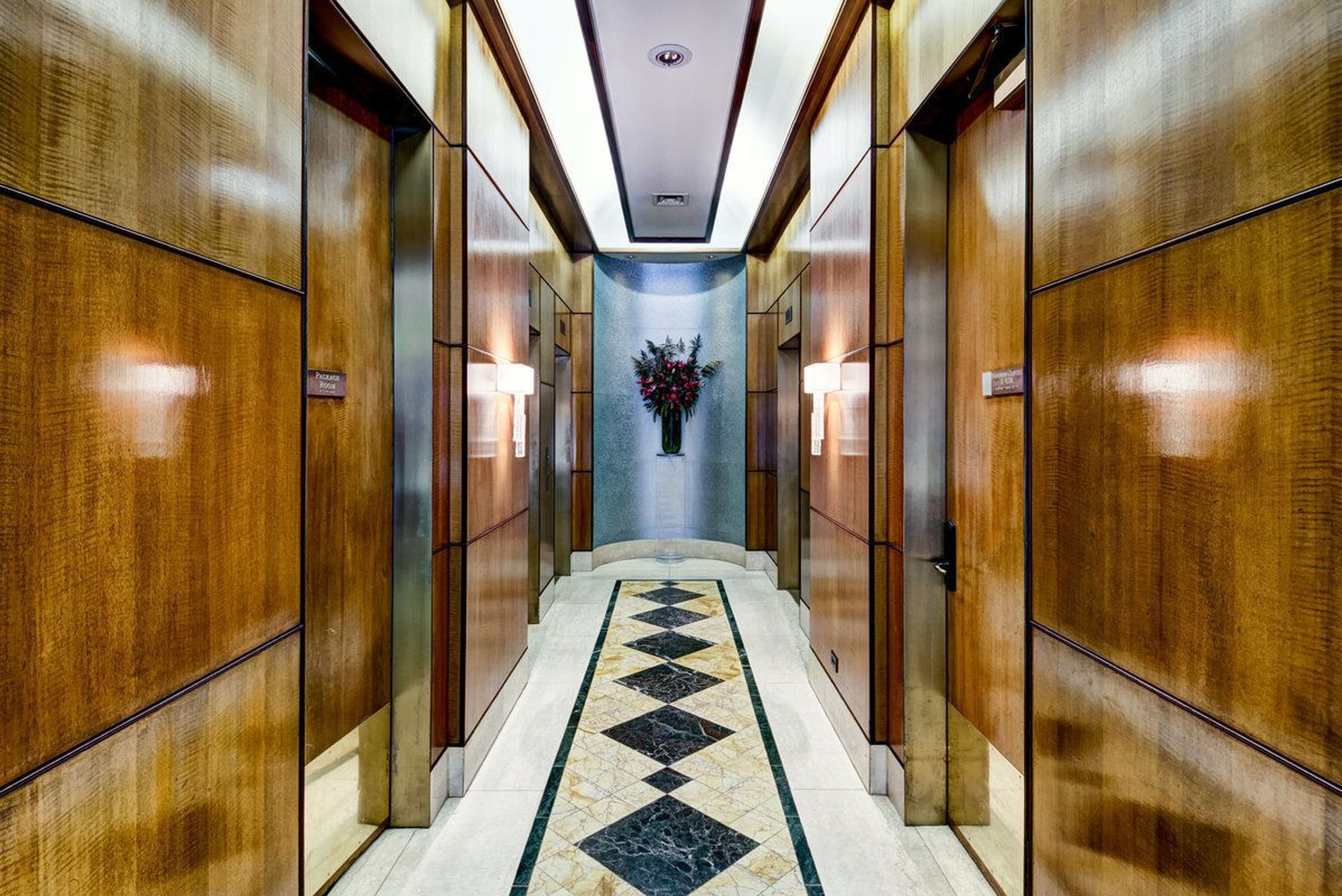 A hallway with wooden paneling, a marble-tiled floor, and a central floral arrangement.