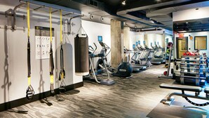 Een sportschool met trainingsapparatuur, een bokszak en een instructieposter aan de muur.