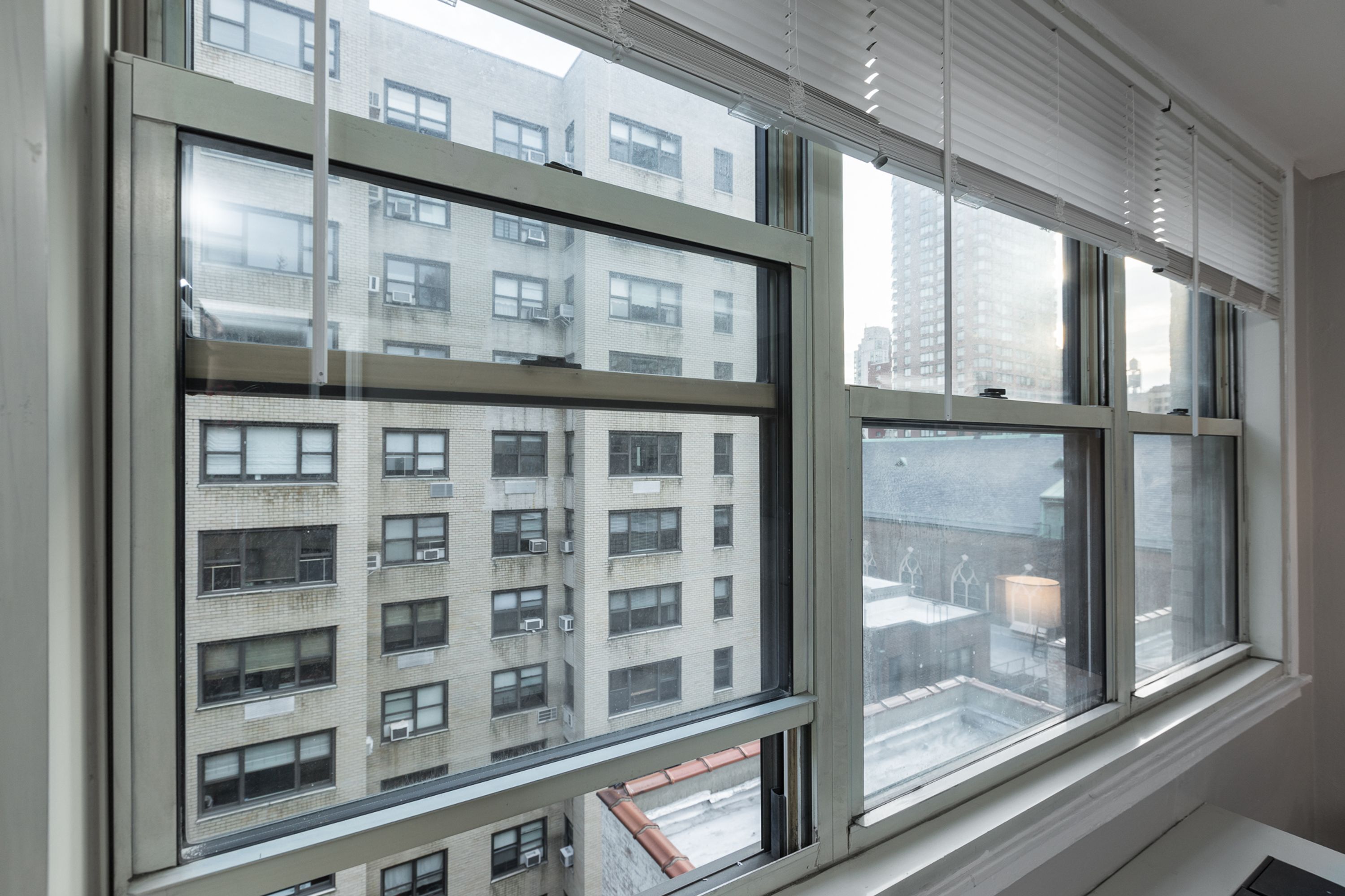 A view through a window of a multi-story building with a modern architectural style, featuring large windows and a visible outdoor area with a table and chairs.