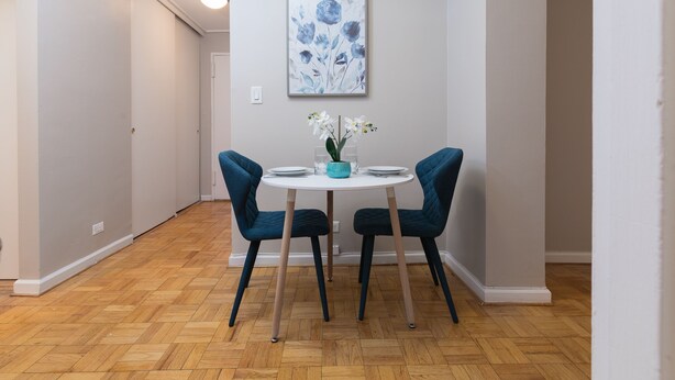 Un coin repas avec une table ronde, deux chaises, un vase de fleurs et un tableau au mur.