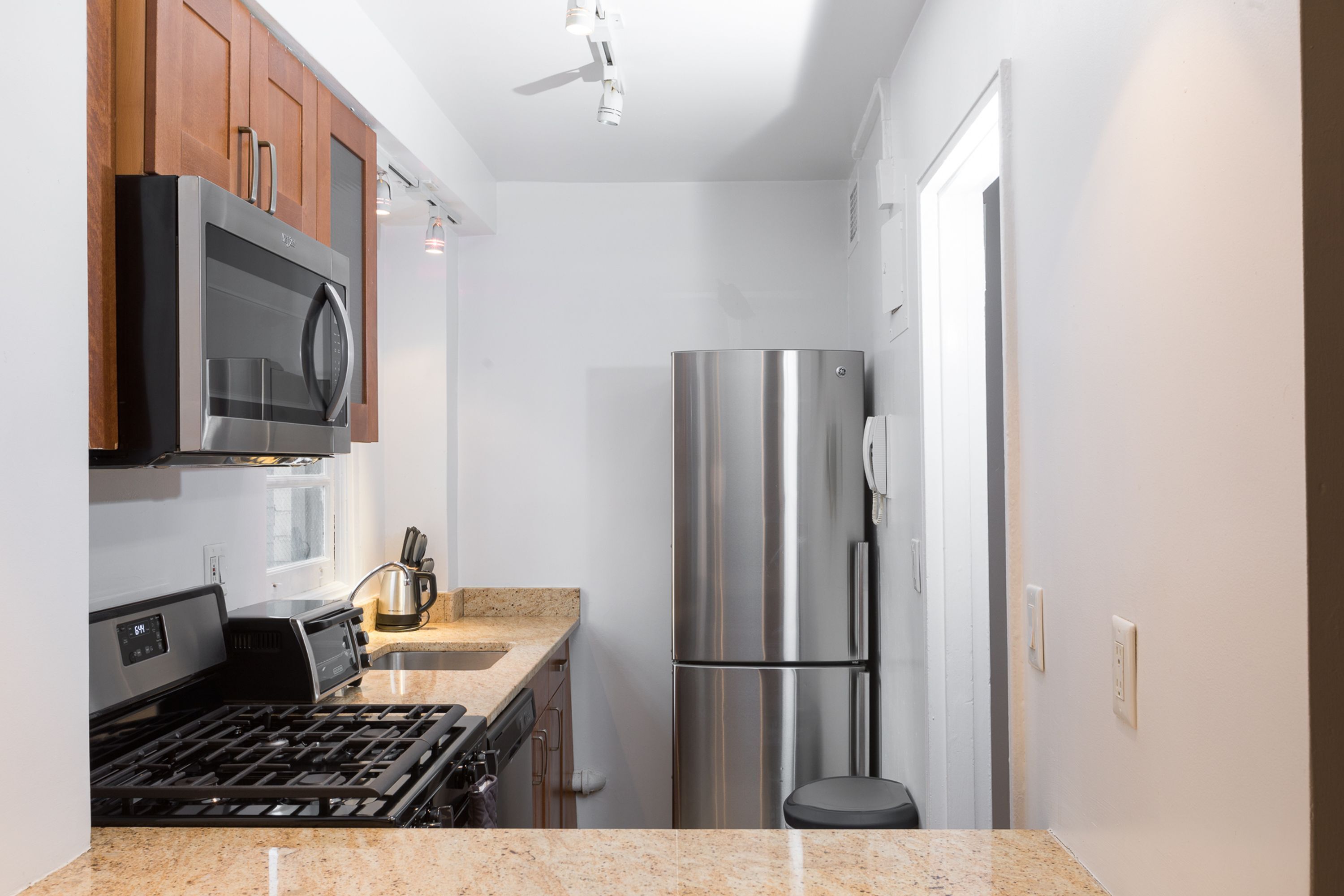 A compact kitchen with a stainless steel refrigerator, a microwave, and a gas stove.
