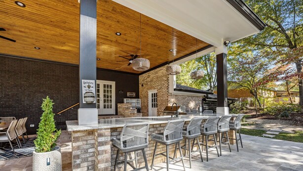 An outdoor bar area with a brick wall, wooden ceiling, and a seating arrangement with metal chairs. - The Retreat at Kincaid (Raleigh)