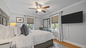 A bedroom with a bed, a ceiling fan, a TV mounted on the wall, and a window with curtains. - The Retreat at Kincaid (Raleigh)