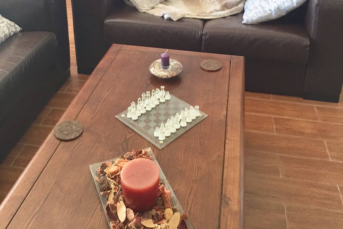 A living room with a brown leather sofa, a wooden coffee table with a candle and a chessboard, and a door with frosted glass panels.
