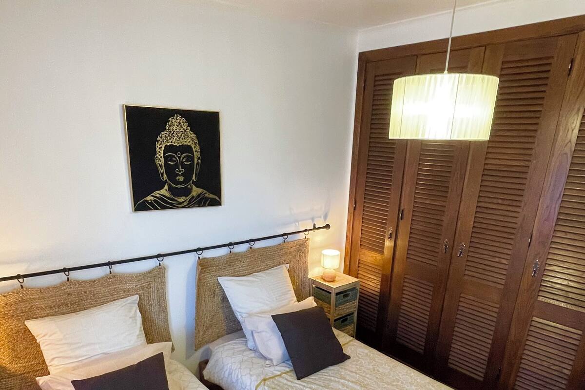 A room with two beds, a Buddha painting, a wooden wardrobe, and a hanging light fixture.