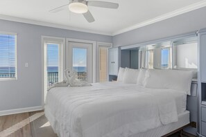 Un dormitorio con una cama grande, un ventilador de techo y vistas a la ciudad desde las ventanas.