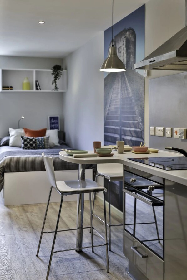 A modern kitchen with a dining area, a bed with a cityscape mural, and a small shelf with decorative items. - Student Only Samuel Tuke (York)