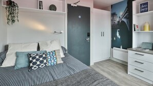 A bedroom with a bed, pillows, a wardrobe, a shelf with decorative items, and a wall with a cityscape mural. - Student Only Samuel Tuke (York)
