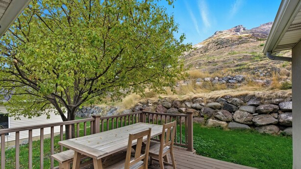 Eine Holzterrasse mit Tisch und Stühlen, umgeben von einer Steinmauer und einem Baum.