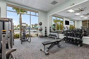 Ein Fitnessraum mit Trainingsgeräten, einer Bank und großen Fenstern mit Blick ins Freie.