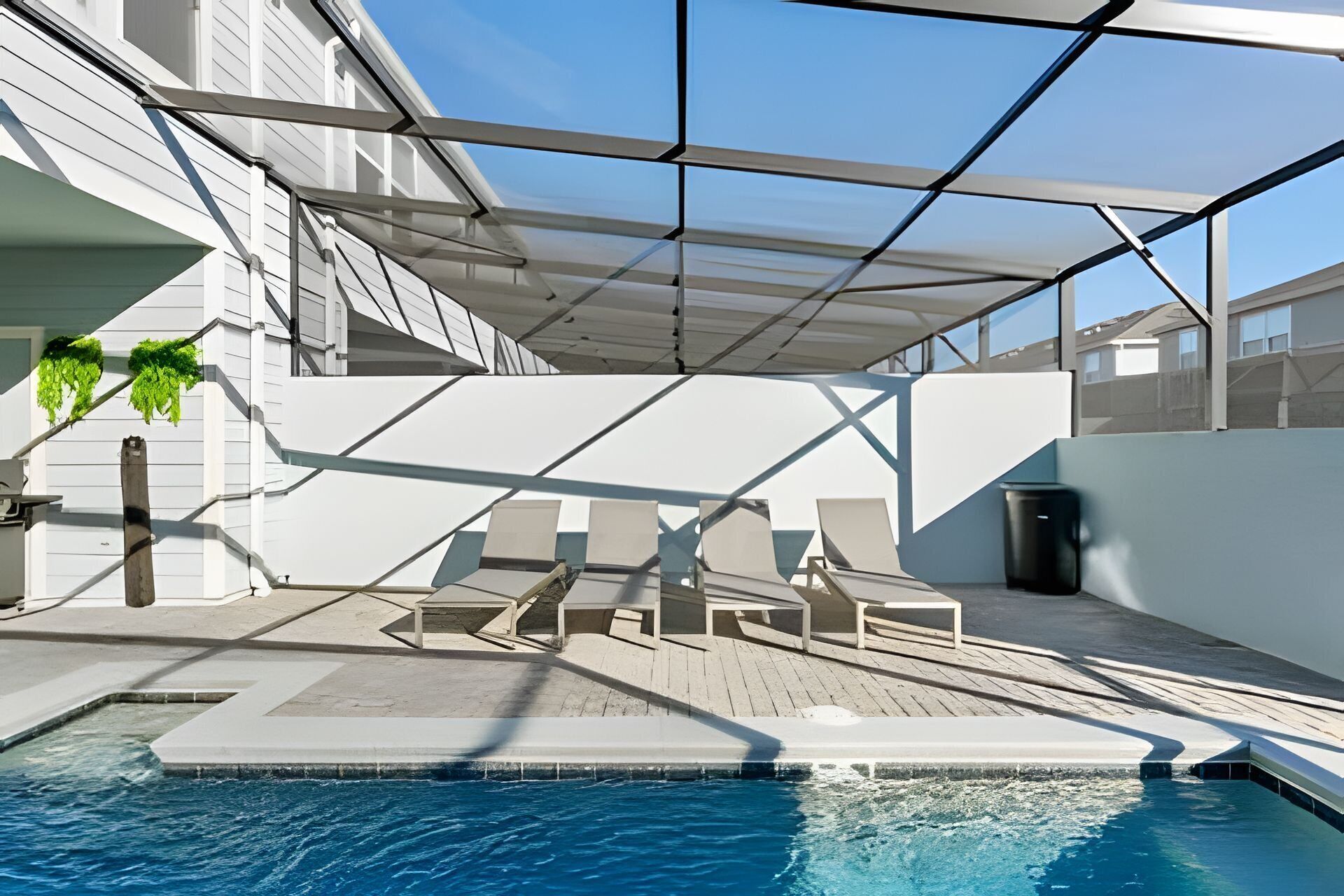 A modern outdoor pool area with a glass enclosure, lounge chairs, and a wooden deck.